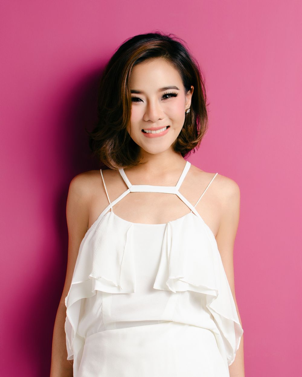 Portrait of someone in a white ruffle top against a pink background, smiling warmly at the camera.