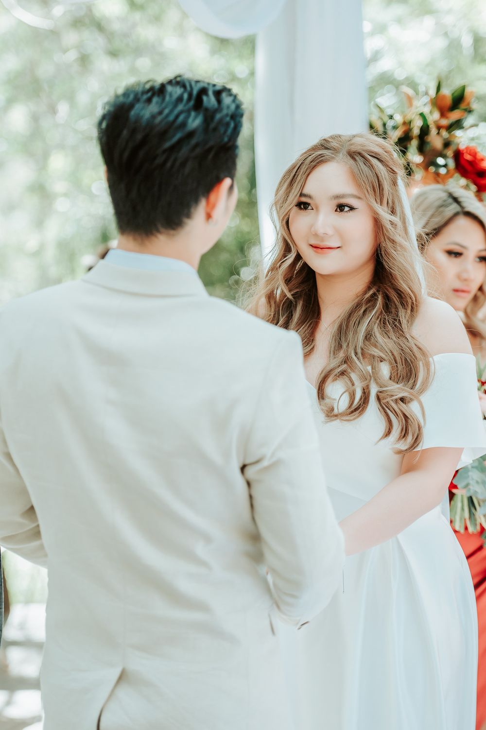 Beautiful wedding ceremony outdoors with couple exchanging vows under white pillars surrounded by floral arrangements.