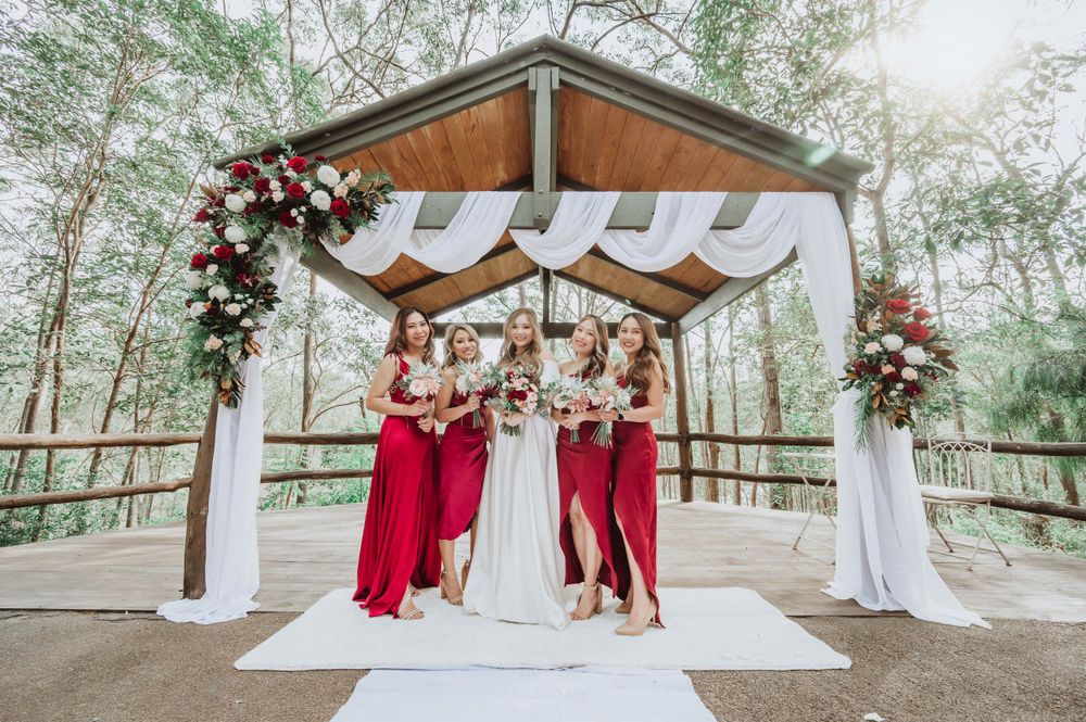 Wedding party poses under an elegant outdoor gazebo decorated with pink floral arrangements and white fabric draping.