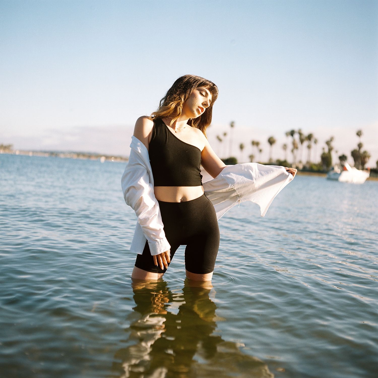 A female model poses in the ocean wearing a dress shirt. Image is captured on the vibrant colors of Kodak's portra film stock