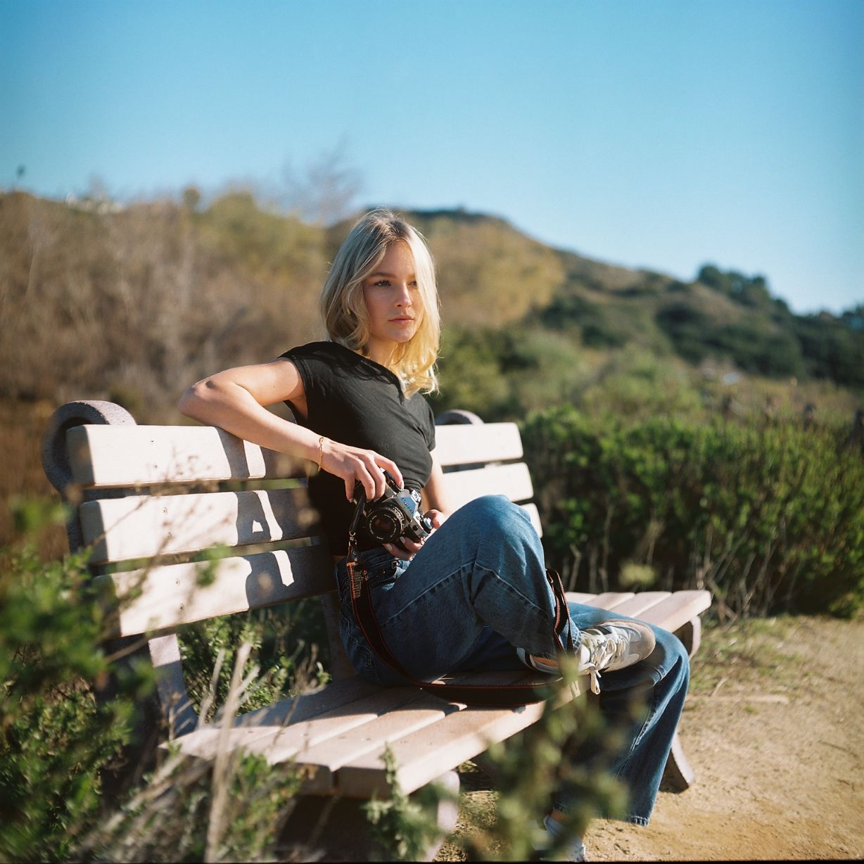 A female model poses on a bench with a camera. Image is captured on the vibrant colors of Kodak's portra film stock