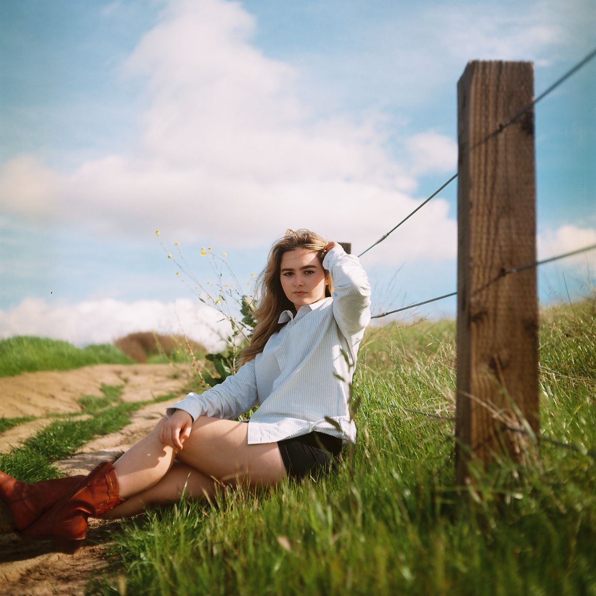 A female model poses in a large field next to a fence. Image is captured on the vibrant colors of Kodak's portra film stock