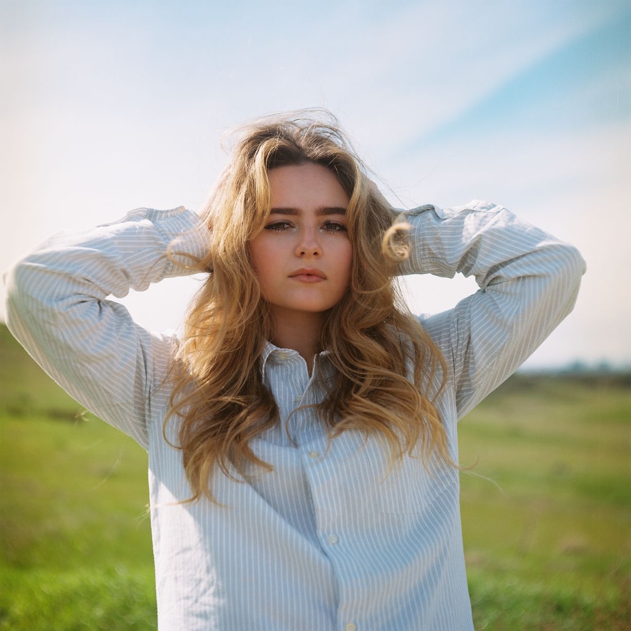 A female model poses in a large open grassy field. Image is captured on the vibrant colors of Kodak's portra film stock