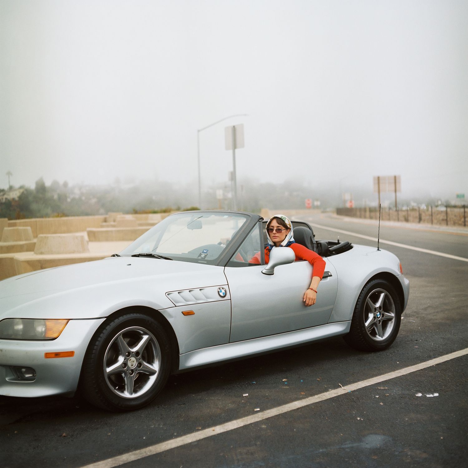 A female model poses in a car with the sun roof down. Image is captured on the vibrant colors of Kodak's portra film stock