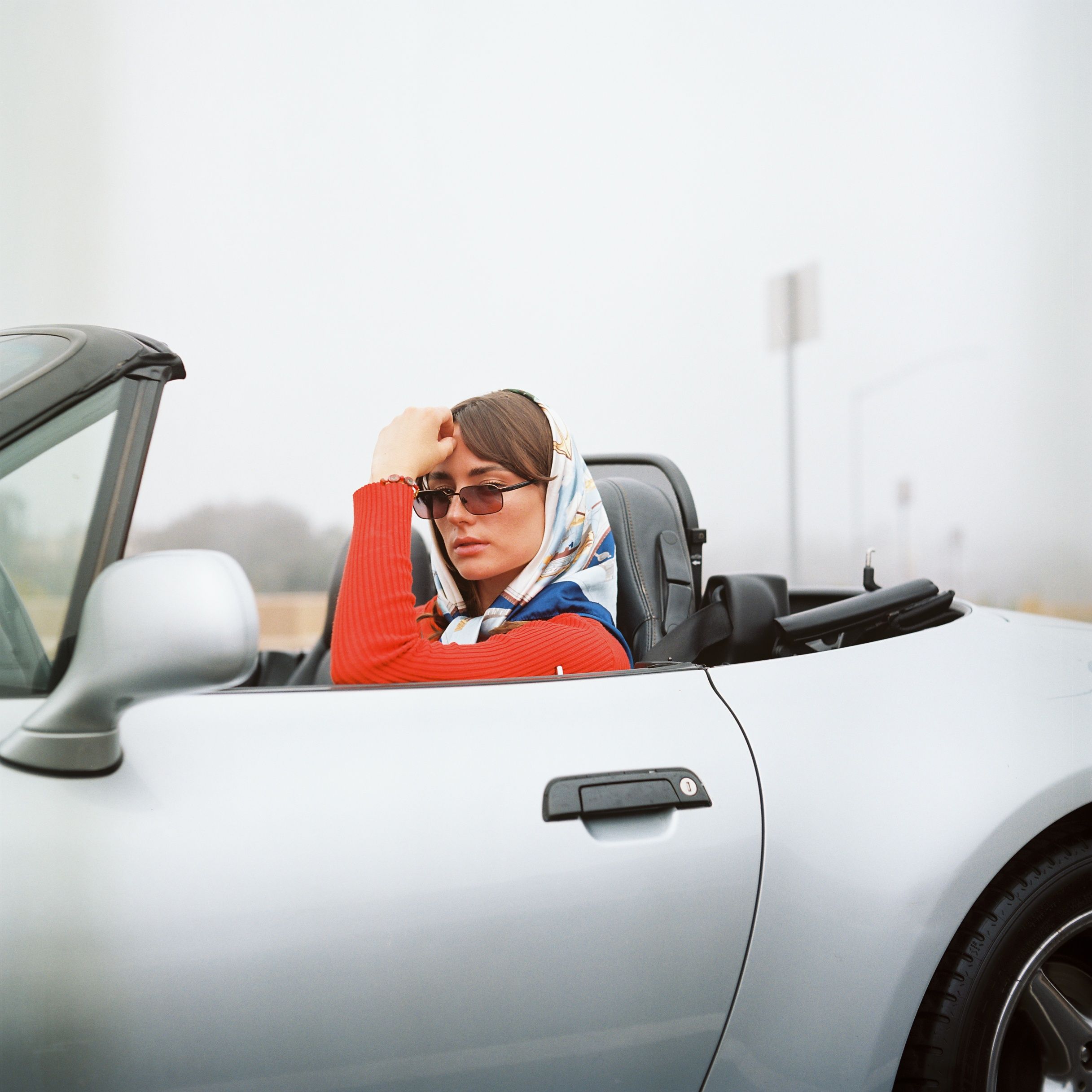 A female model poses in a car with the sun roof down. Image is captured on the vibrant colors of Kodak's portra film stock