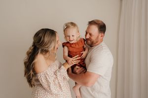 A family shares a tender moment together against a neutral wall backdrop in natural lighting.