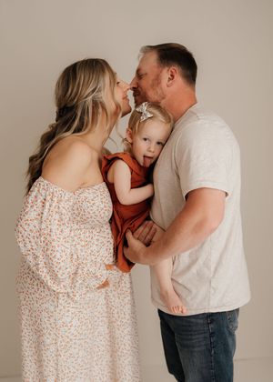 A family shares tender moments in a studio photoshoot wearing white and floral dress against neutral backdrop.