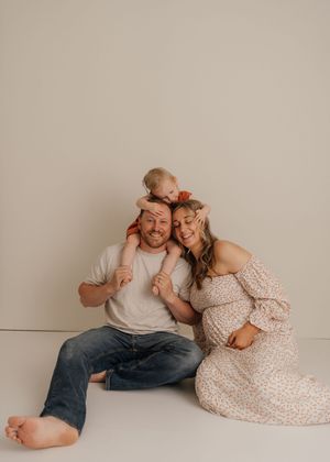 On a neutral background, couple lying on floor in white and beige outfits sharing intimate playful poses.