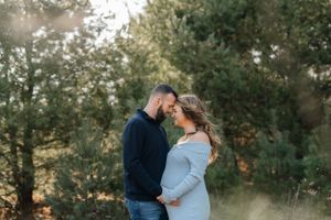 Romantic maternity photo of couple sharing intimate moment among pine trees.