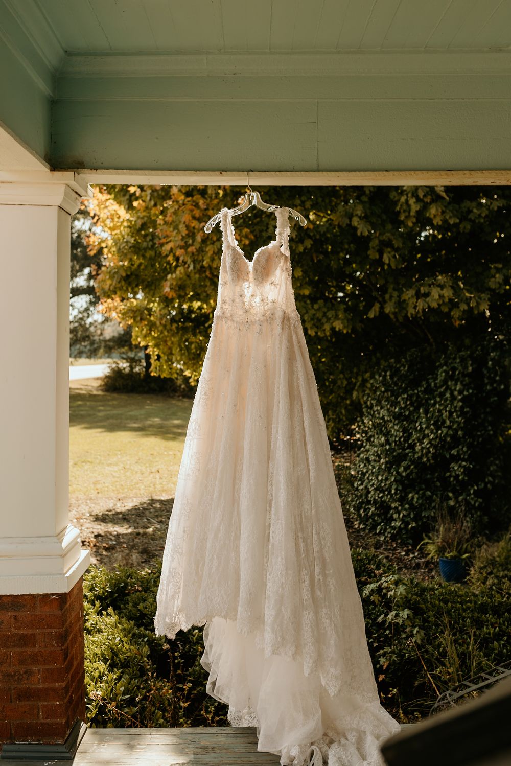 Photograph of an elegant lace wedding dress hanging on porch at Wild Daisy Farm in Molena, Georgia.