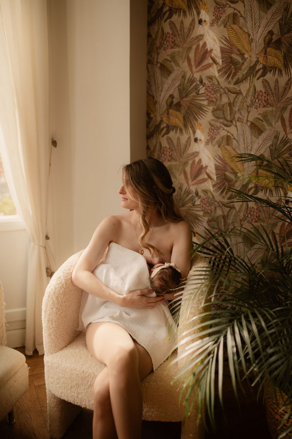Une maman qui allaite sa petite fille dans une ambiance douce et chaude pendant la séance photo naissance à Grasse.
