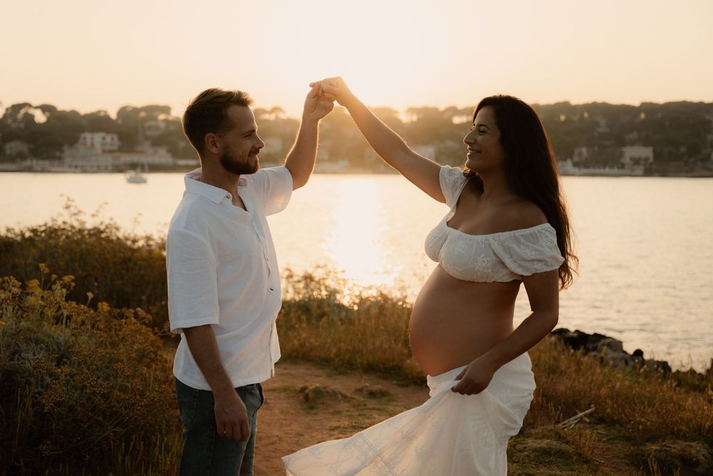 Un couple danse au coucher du soleil tandis que la femme laisse apparaitre le ventre rond de sa grossesse.