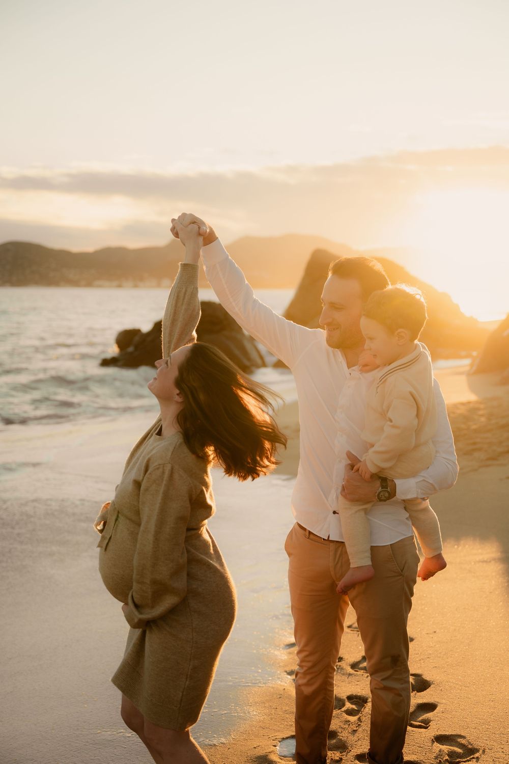 Papa qui tient son premier enfant dans ses bras et fait danser sa femme enceinte au bord de mer à la plage des rochers à La Bocca.