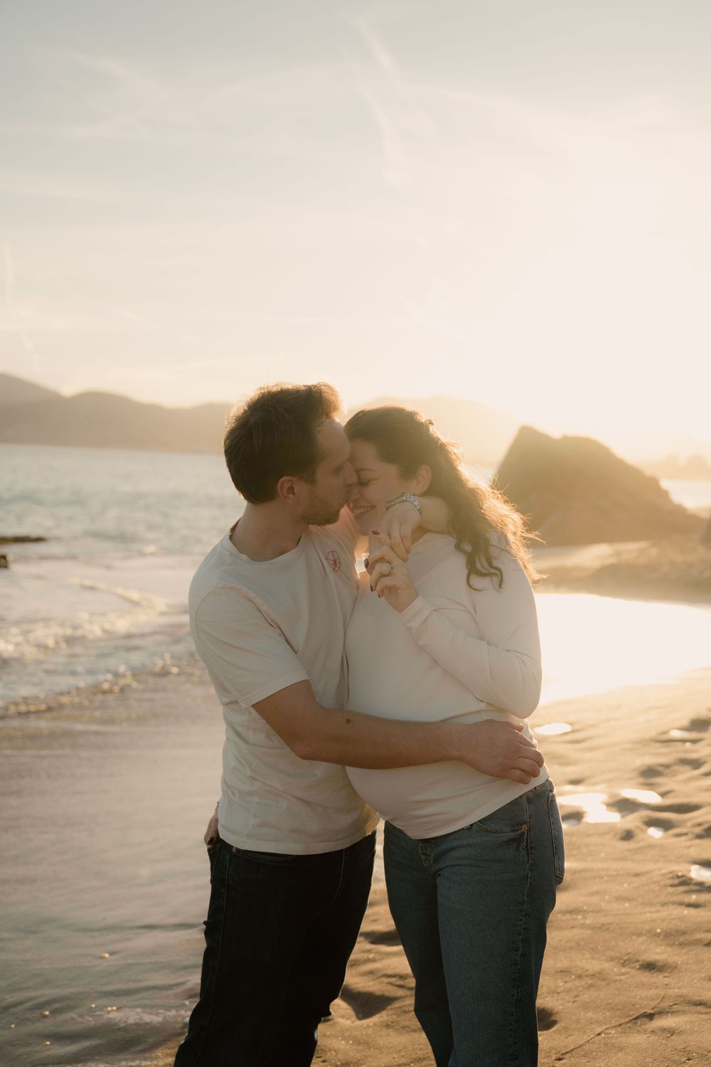 Séance photo au coucher du soleil sur une plage de cannes, un homme embrasse le nez de sa femme enceinte