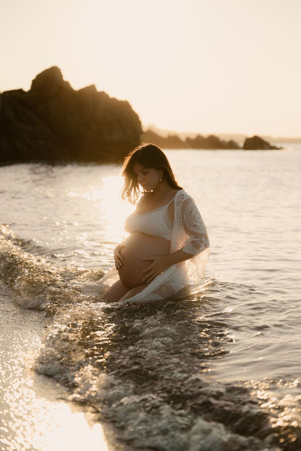 Futures maman assise en maillot blanc et paréo en bord de mer à Cannes au levé du soleil.