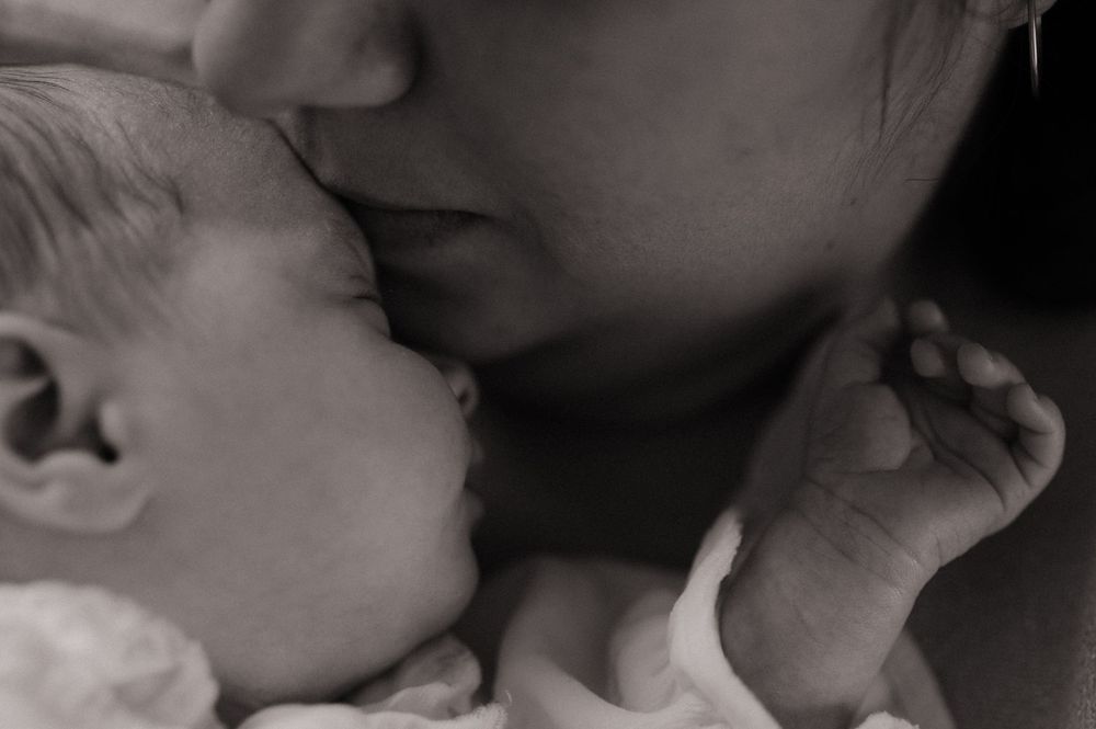 Gros plan du bas du visage d'une maman qui sent son bébé contre elle.