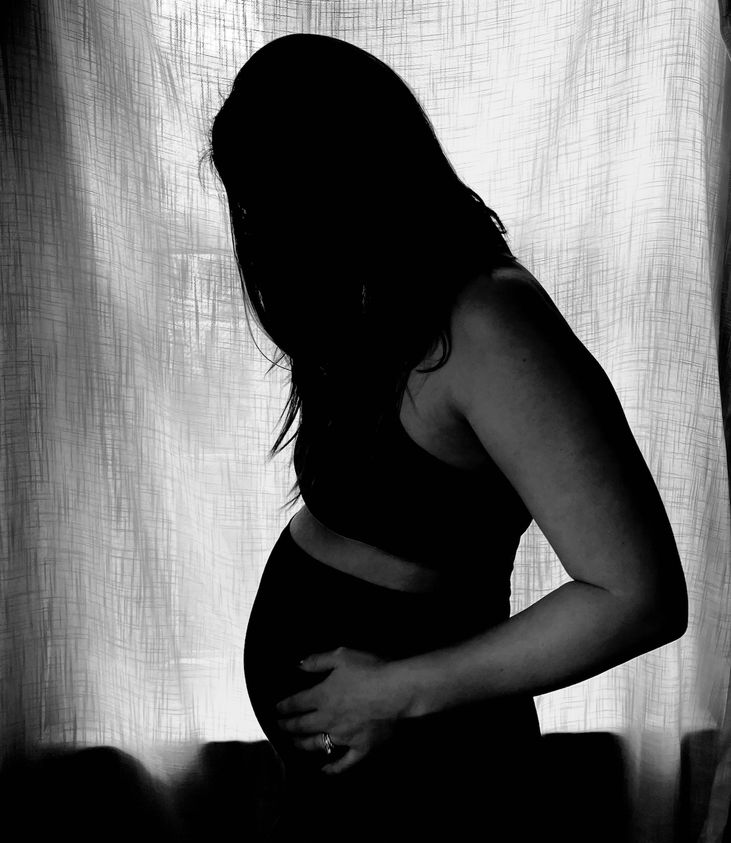 Black and white silhouette of an expectant mother's side profile with hands cradling her pregnant belly.