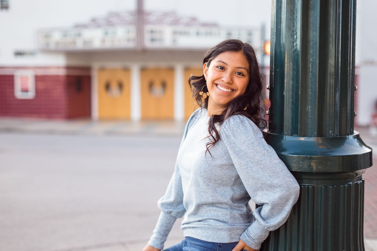 Casual senior portrait session against a vintage green column in an urban setting.
