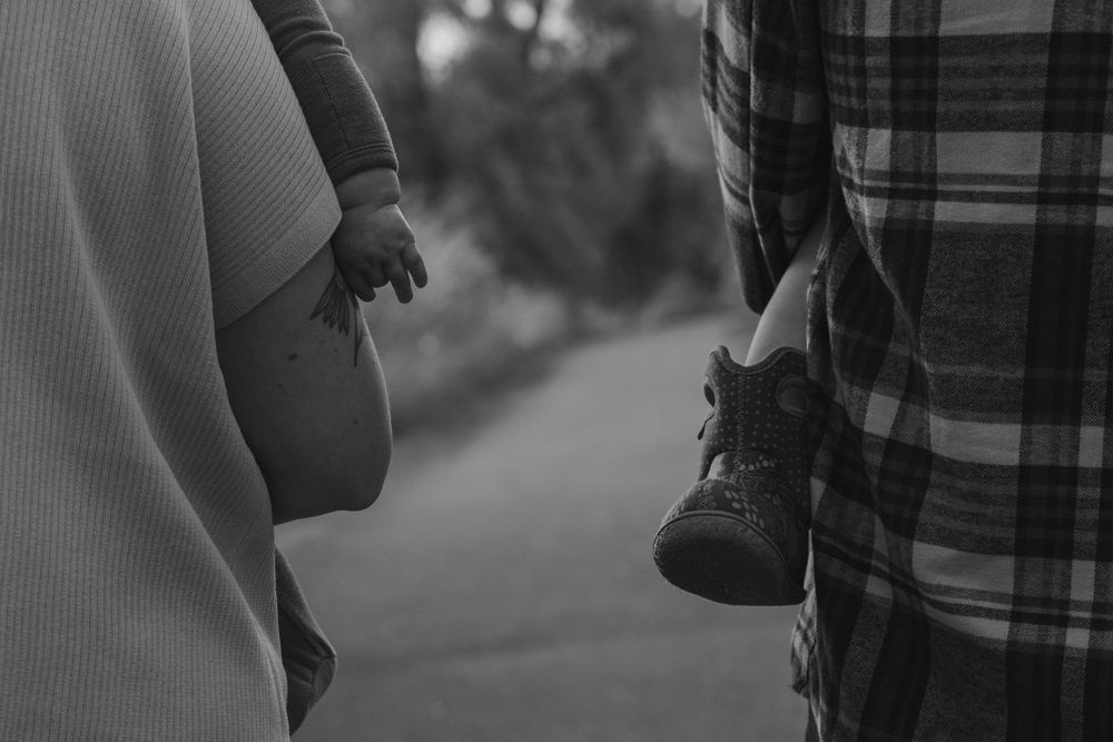 A black and white silhouette shows someone holding a small child's shoes.