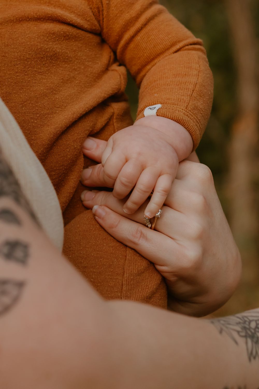 Close-up of hands holding a baby's hand with a ring visible and orange clothing in warm lighting.
