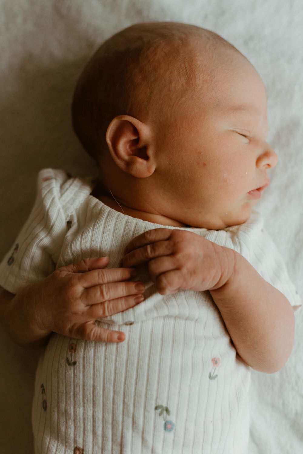 A close-up sequence shows a newborn baby in a white knit cardigan lying on soft white bedding.