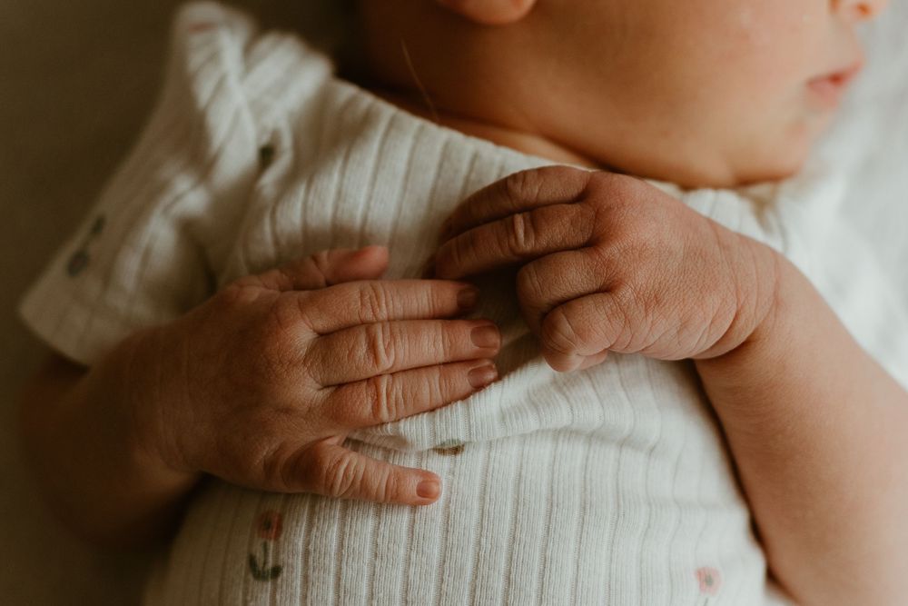 A close-up sequence showing gentle hands holding and caressing a newborn baby wearing a white knitted sweater.