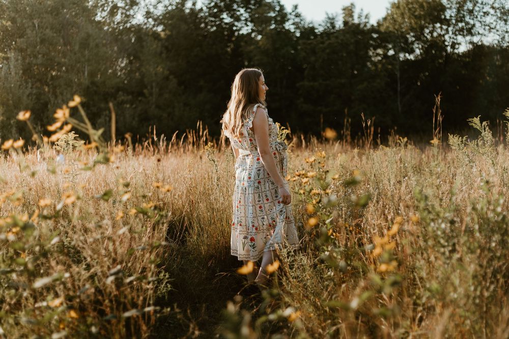 Woman in a long white dress walks through a golden meadow at sunset during a romantic countryside photoshoot.