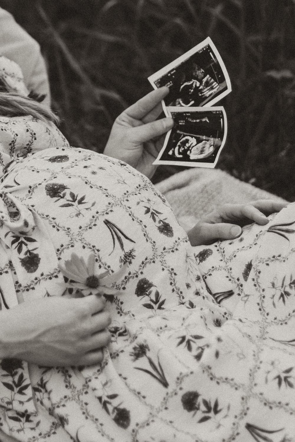 Hands holding black and white ultrasound photos on a floral patterned fabric background.