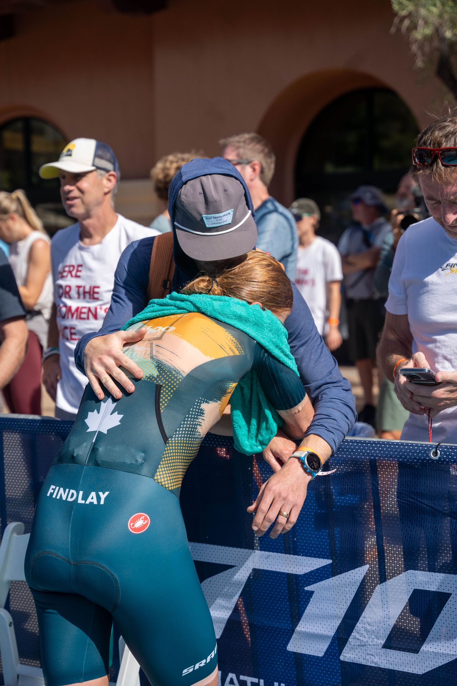 A cyclist adjusts their position on a triathlon bike during a competition setup with a turquoise backdrop.