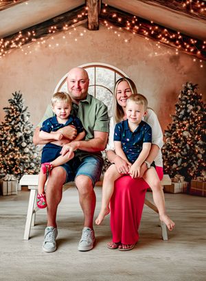 Family of four smiling in front of Christmas trees with festive lights in a cozy holiday photo session.