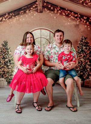 Family of four in matching floral outfits posing for a Christmas photo with decorated trees and fairy lights.