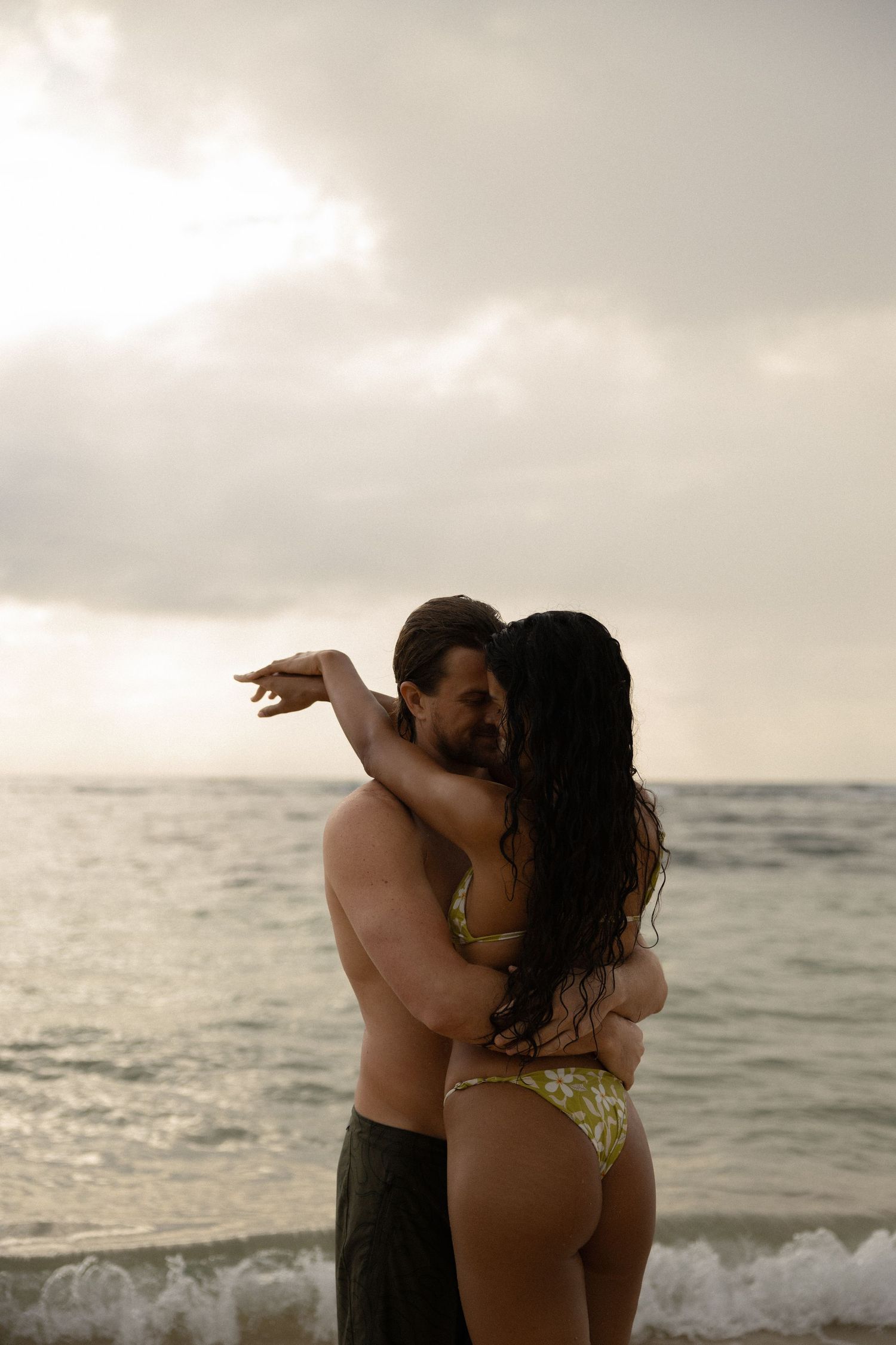 A couple embraces on the beach during sunset near ocean waves.