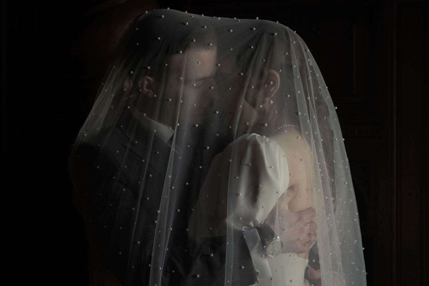 A veiled figure stands in dramatic lighting against a dark background with glittering sparkles on the translucent fabric.