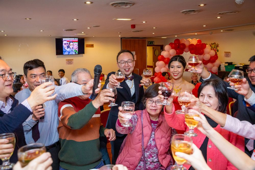 Wedding guests raising glasses in a joyful toast with bride and groom at a Chinese wedding banquet.