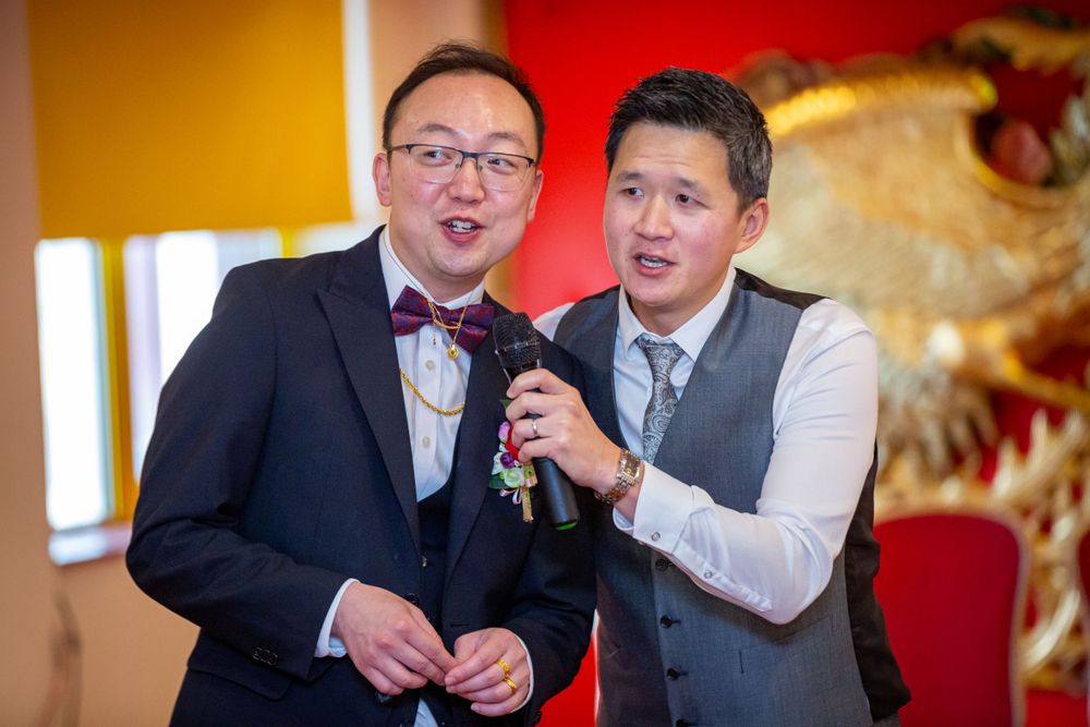 Groom and best man sharing a fun moment with a microphone at a Chinese wedding reception.