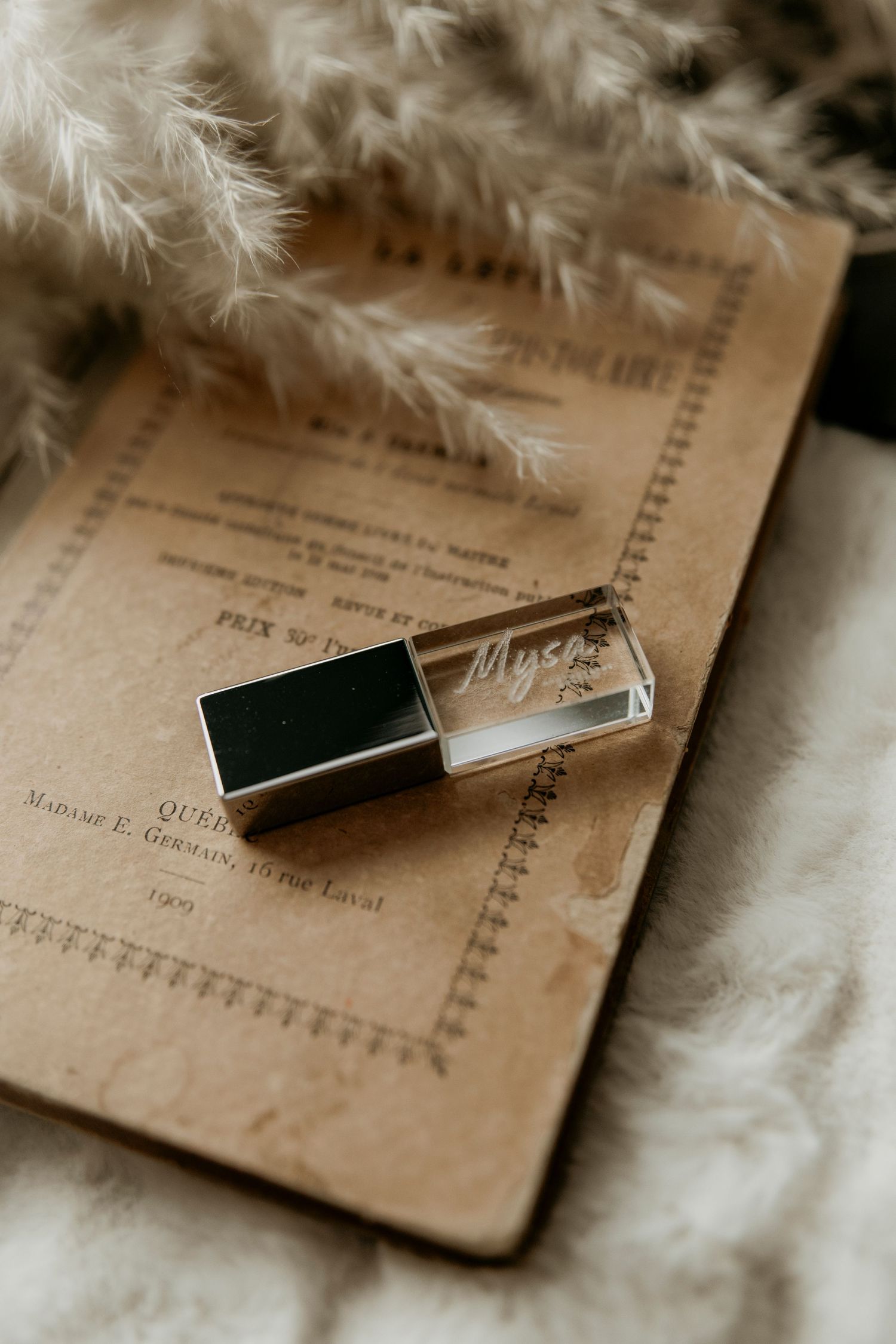 A vintage glass USB drive rests on an aged paper document with soft white feathers in the background.