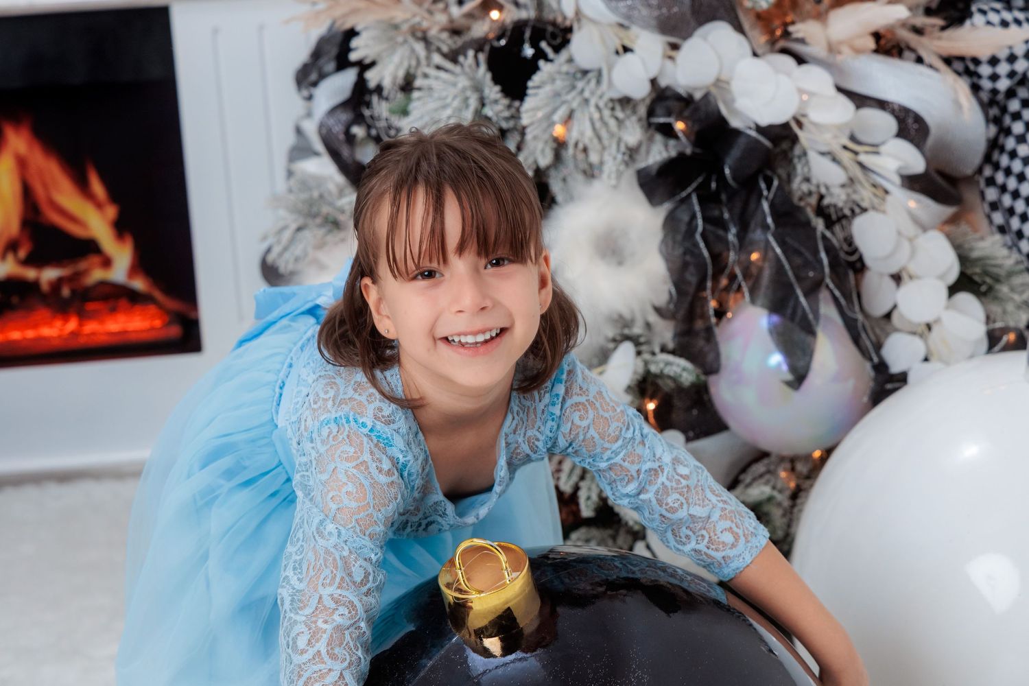 Child in a plaid dress and blue tulle skirt poses playfully in a festive holiday setting.