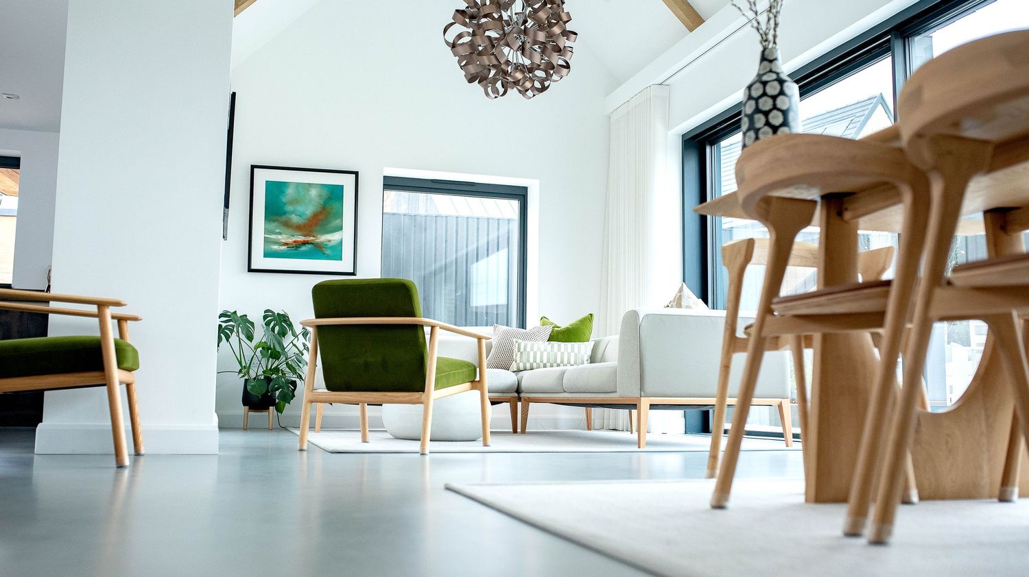 Modern living room interior with green accent chairs, wooden furniture and bright natural lighting.