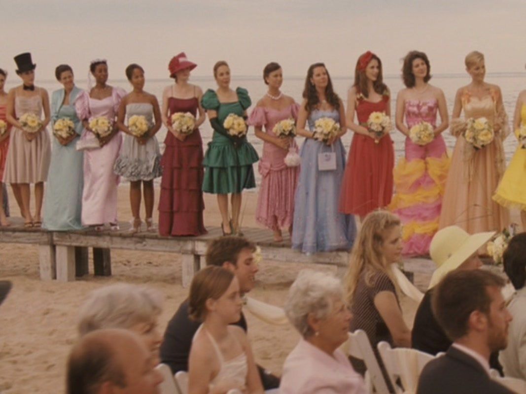 Bridal party wearing mismatched pastel and colorful dresses standing in a row at beach wedding.