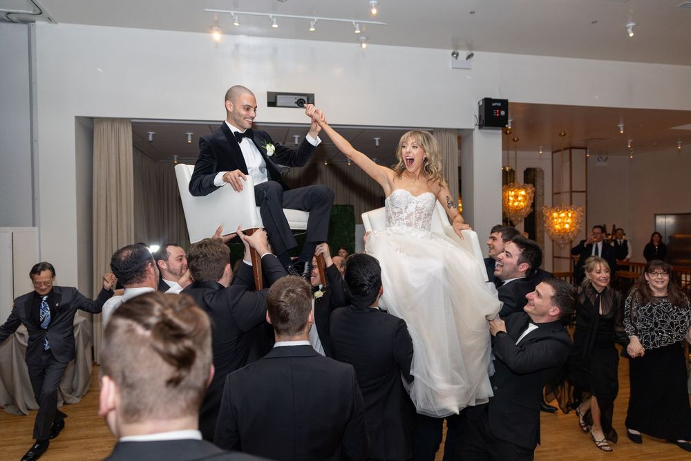 A wedding couple performs their first dance surrounded by guests in an elegant ballroom reception venue.