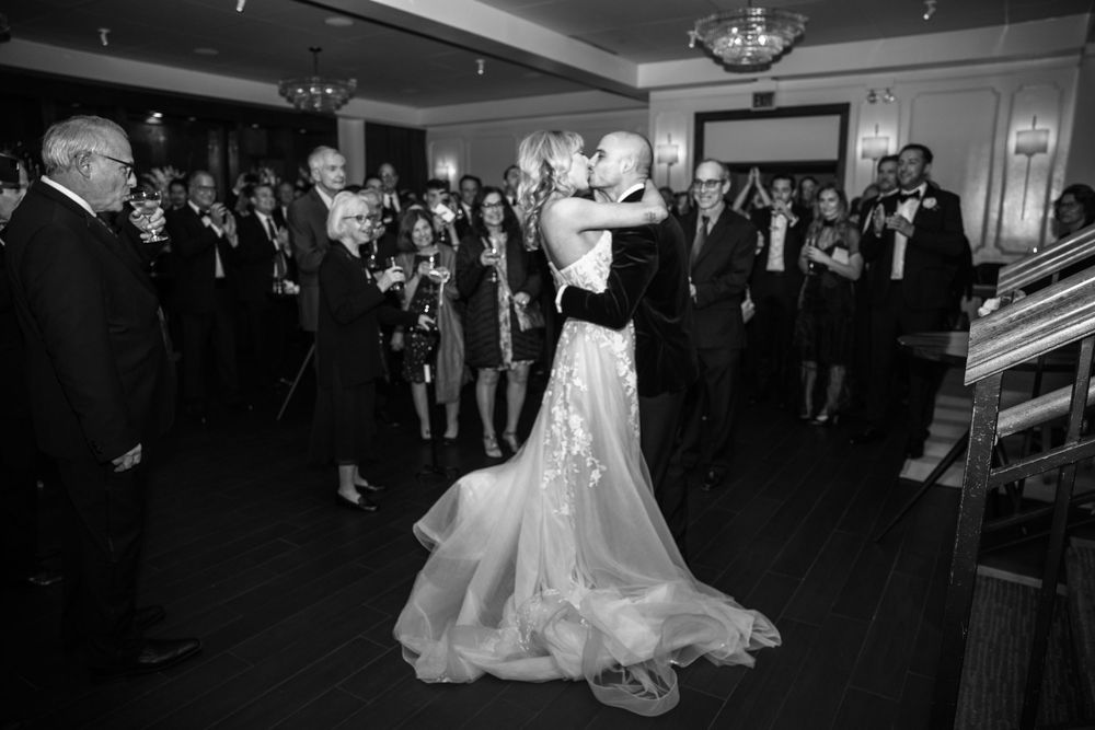 A couple performs an elegant ballroom dance move in formal attire at an evening event with onlookers.