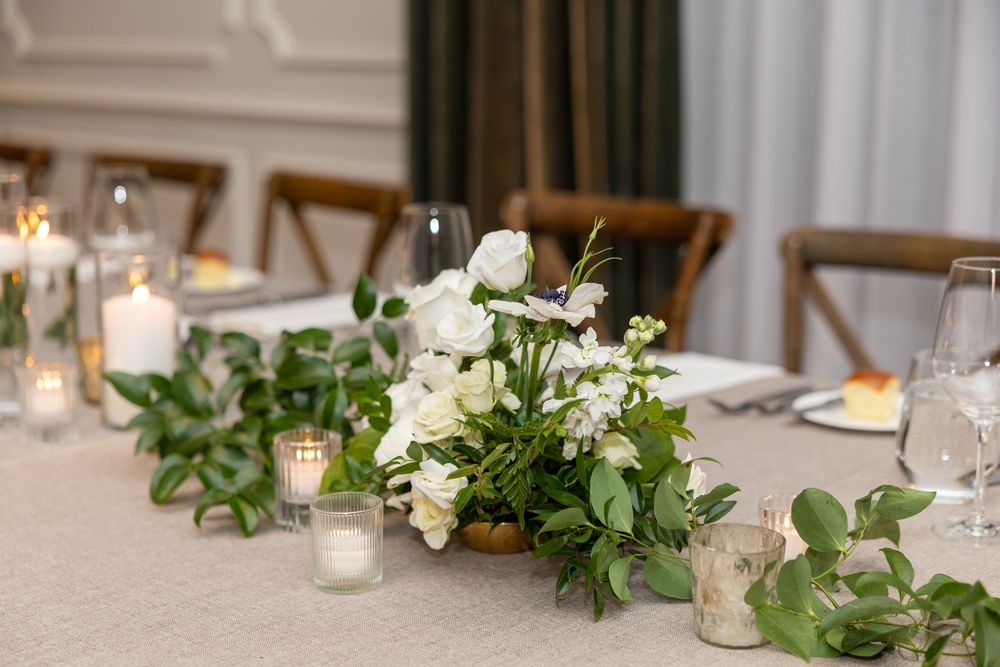 Elegant wedding reception table decorated with greenery garlands, white candles and delicate floral arrangements.