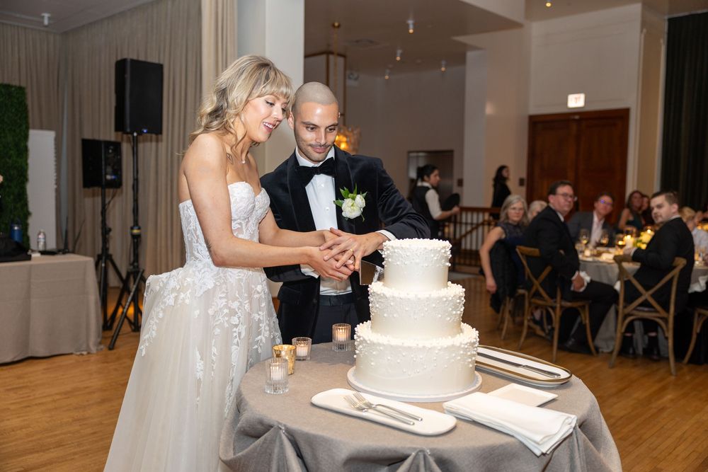 A couple cuts their elegant white wedding cake together at an indoor reception venue.