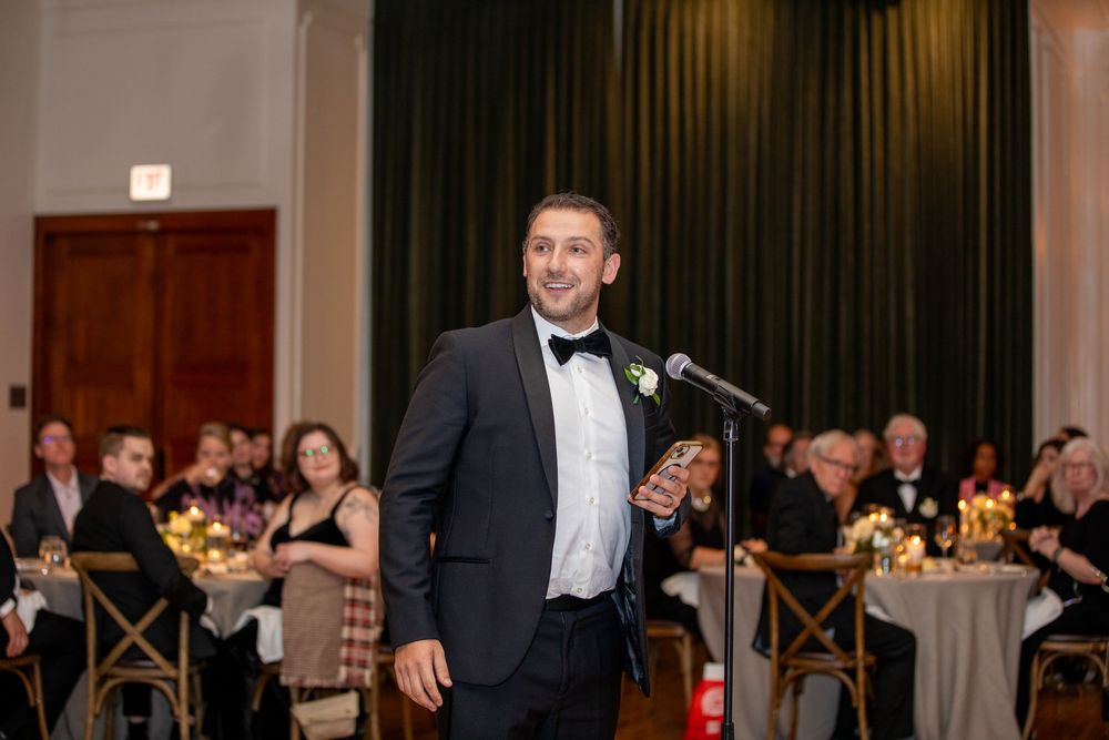Guests enjoying a formal reception in an elegant ballroom with chandeliers and dark curtains.