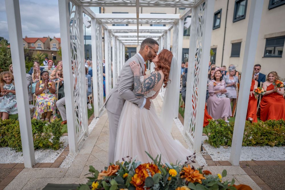 A wedding celebration moment captured in a white outdoor pergola with colorful flowers.