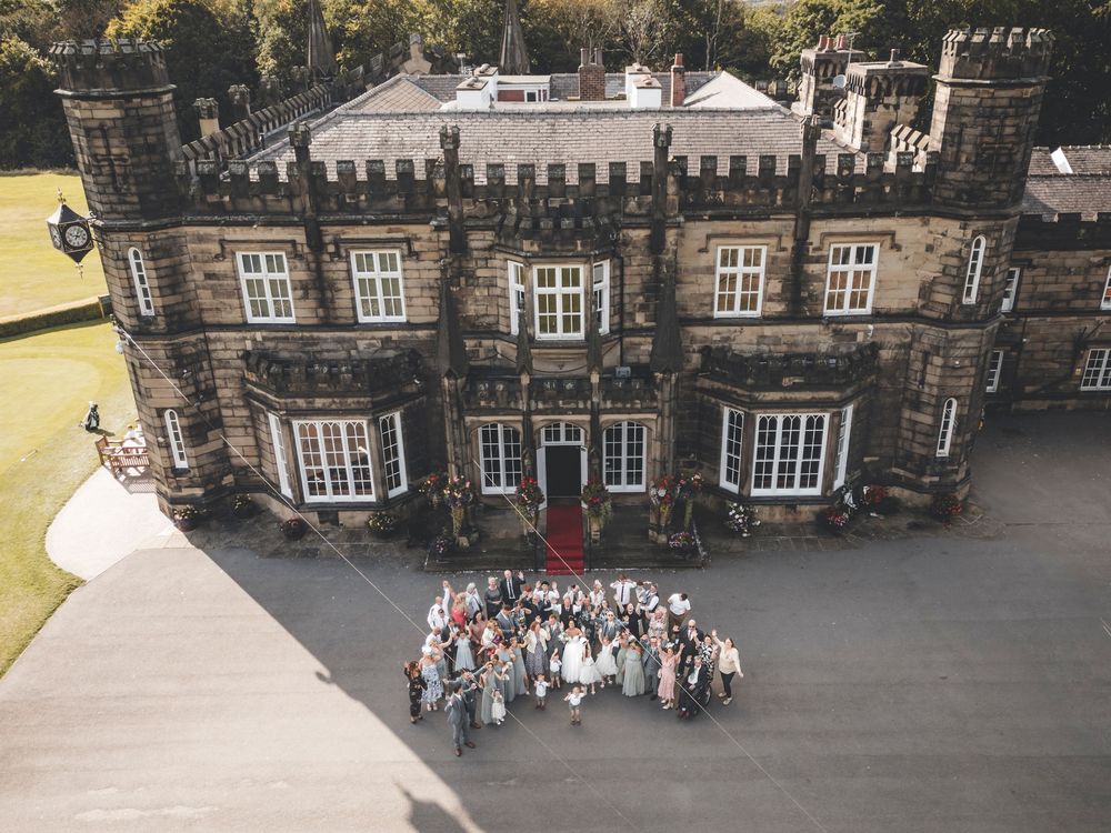 Aerial view of wedding party gathered outside historic stone castle.