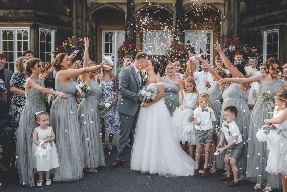 Wedding party and guests celebrate with confetti toss outdoors.