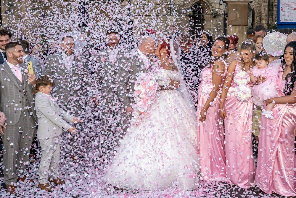 Wedding party celebrates with confetti shower against pink and grey color scheme.