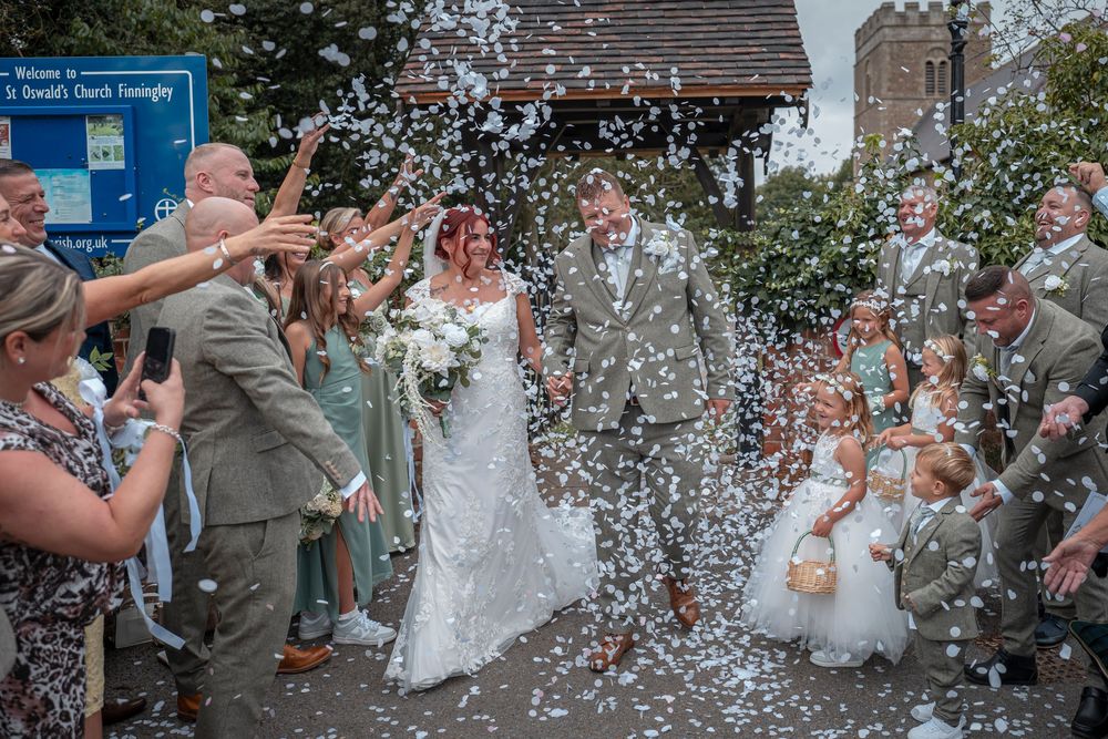 Wedding party walking through shower of white confetti outdoors.