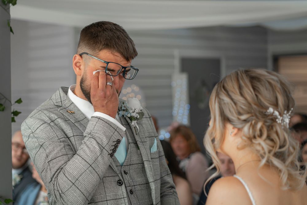 Emotional moment during wedding ceremony in grey suit and white dress.